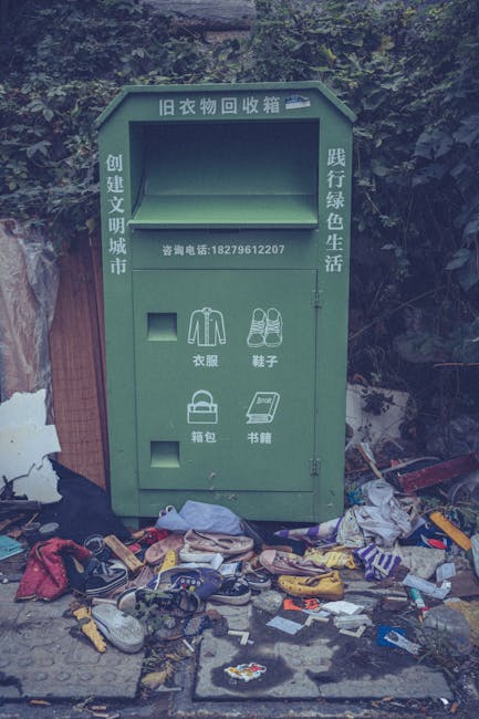 A close-up view of a densely packed collection of household waste materials scattered across a surface, consisting mainly of crumpled and torn paper, cardboard packaging, and plastic bottles. The paper items vary in texture, some appearing smooth while others are wrinkled or shredded, with a mix of plain and printed surfaces. Several transparent plastic bottles with visible labels and caps are strewn across the pile, exhibiting glossy textures and slight distortions from crumpling. Cardboard boxes and packaging materials, some with printed branding, are partially flattened and layered on top of each other, adding to the cluttered scene. The overall color tone of the image is neutral and muted, with shades of gray, black, and white, consistent with a monochrome depiction of waste. The background shows an indistinct environment that could be an outdoor or indoor space used for waste collection or disposal, with no visible machinery or cleaning tools present. This image from Waste Disposal Kennington highlights the typical clutter associated with private rubbish removal or on-site clearance tasks, emphasizing the need for proper waste handling and disposal practices in line with local regulations.
